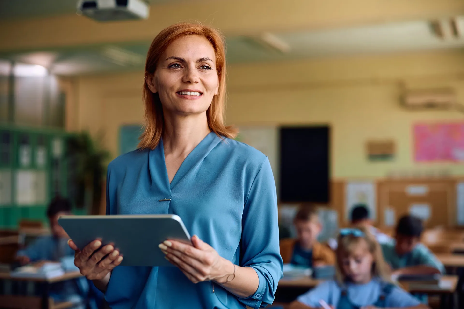 A smiling teacher holding a tablet in a classroom